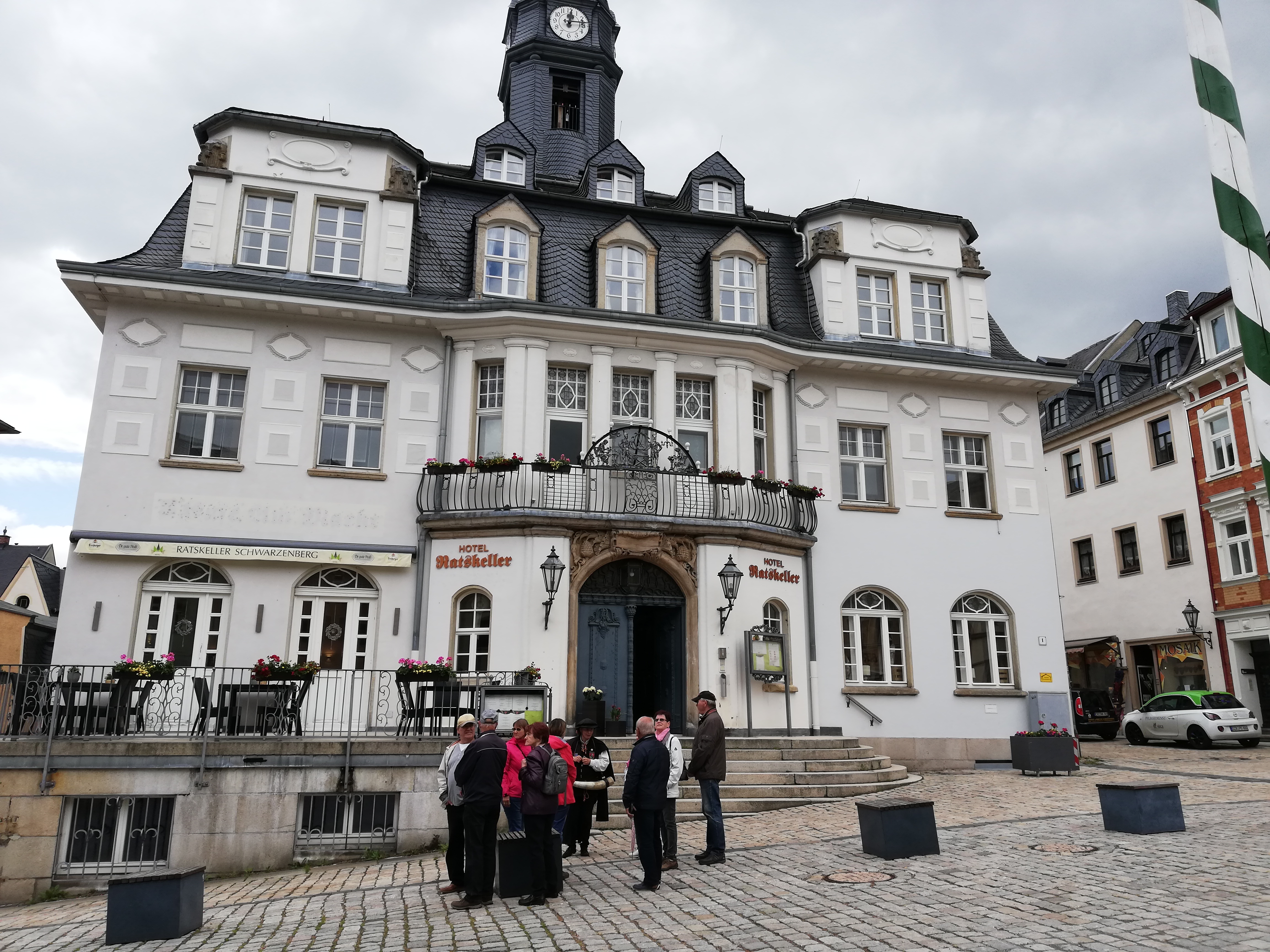 Die Teilnehmer an der Stadtführung stehen in der Schwarzenberger Altstadt vor dem Hotel "Ratskeller" mit Balkon und Turmuhr